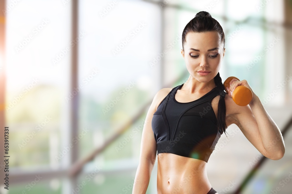 Young sporty woman exercising with gym dumbbells
