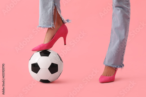 Legs of young woman wearing high heels and playing with soccer ball on pink background