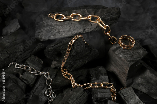 Beautiful chain bracelets and ring on black charcoal, closeup