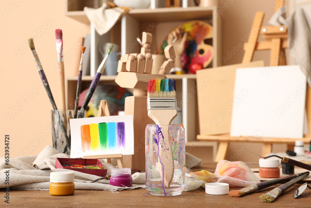 Glass with brushes, paints and mini easel in artist's studio Glass with brushes, paints and mini easel in artist's studio