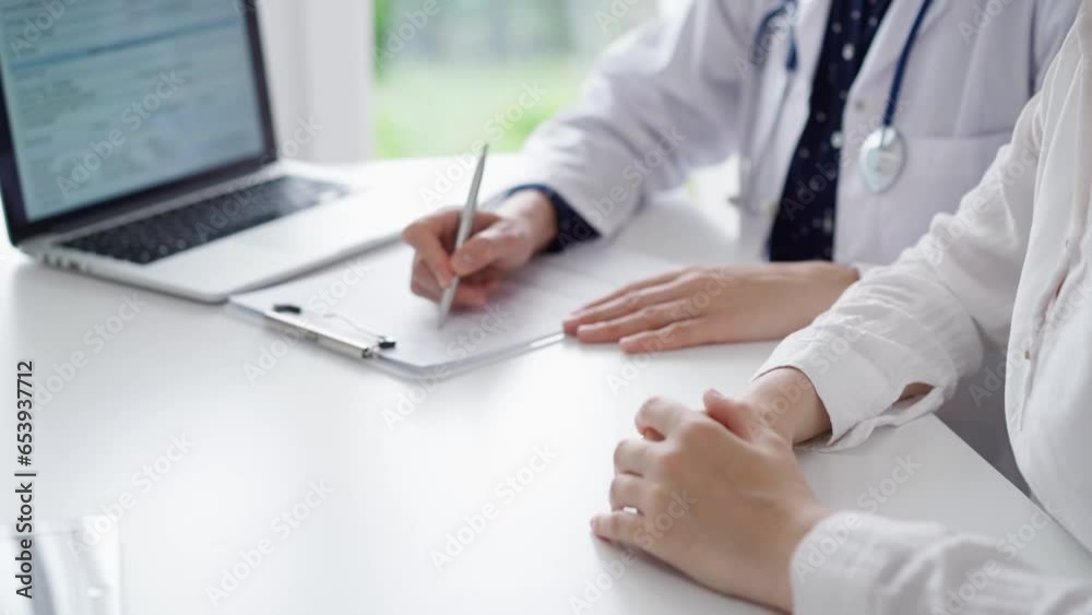 Doctor and patient sitting at the table and talking. The pediatrician in a blue dotted blouse and white medical coat is writing something on a clipboard. Medicine, healthcare concepts Doctor and patient sitting at the table and talking. The pediatrician in a blue dotted blouse and white medical coat is writing something on a clipboard. Medicine, healthcare concepts