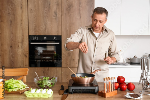 Fotografia Mature man spicing fried vegetables in kitchen