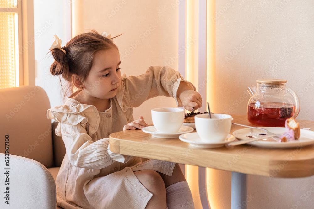 Cute little brunette girl drinking a tea with spoon at the table and eating some cookies. Family weekend. Happy spare time. High quality photo Cute little brunette girl drinking a tea with spoon at the table and eating some cookies. Family weekend. Happy spare time. High quality photo