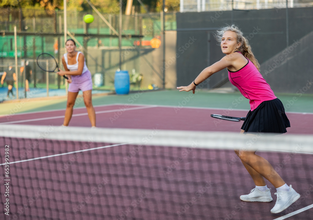 Caucasian young woman in tank top and skirt playing tennis match during training on court.