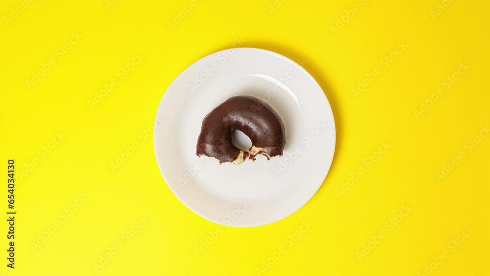 Eating delicious sweet donut covered with chocolate glaze on bright yellow background. Stop motion food donut animation video. Bakery and food concept. Top view of chocolate doughnut in 4K