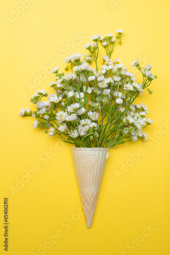 bouquet of wildflowers daisies in an ice cream cone on a yellow background.Flat top view. © Ann Stryzhekin
