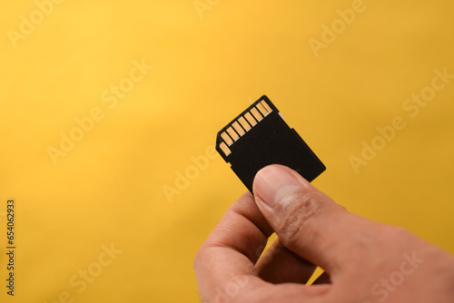 Hand holds SD Card for DSLR or Mirrorless camera on yellow background