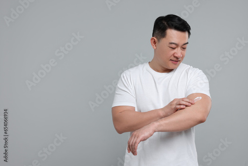 Handsome man applying body cream onto his arm on light grey background. Space for text