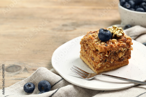 Piece of delicious layered honey cake with blueberries and nuts served on wooden table, closeup. Space for text