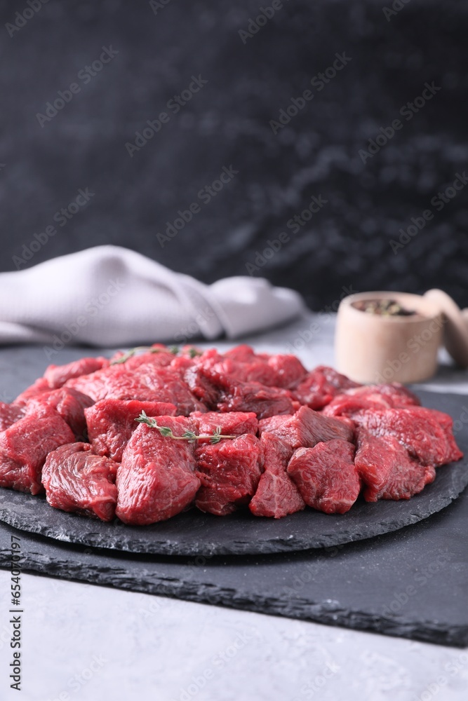 Pieces of raw beef meat and thyme sprigs on grey textured table. Space for text Pieces of raw beef meat and thyme sprigs on grey textured table. Space for text