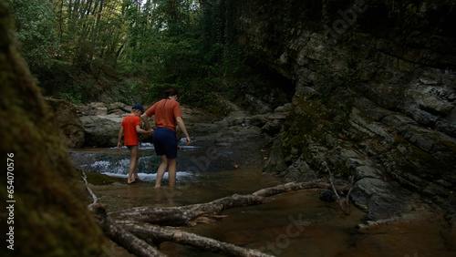 Boy and mother walking among rocks in cold stream. Creative. Hiking in wild nature.