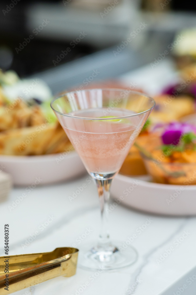 pink cosmopolitan cocktail sitting on bar in restaurant with platters of appetizers in the background 