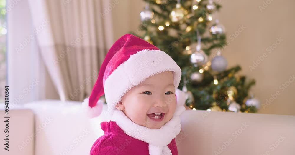 portrait of happy Asian baby child in Santa hat and red costume smiling having fun while standing in Christmas interior at home, Kid wearing Christmas red hat and dressed in cute holiday clothes portrait of happy Asian baby child in Santa hat and red costume smiling having fun while standing in Christmas interior at home, Kid wearing Christmas red hat and dressed in cute holiday clothes