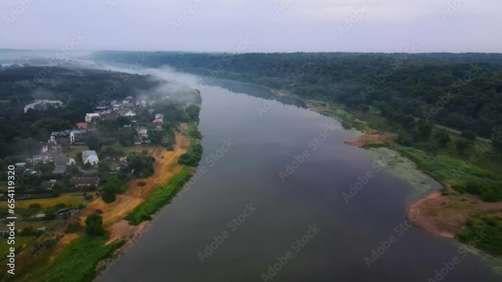drone shot of a wide Nemunas river with a green forest and houses on the bank on a cloudy day. There is fog over the river in the background drone shot of a wide Nemunas river with a green forest and houses on the bank on a cloudy day. There is fog over the river in the background