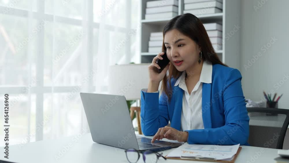 Attractive Asian businesswoman Use your laptop to watch your computer and talk on the phon. Consult customers, sit at a table. financial officer making a mobile business call Discuss work with clients Attractive Asian businesswoman Use your laptop to watch your computer and talk on the phon. Consult customers, sit at a table. financial officer making a mobile business call Discuss work with clients