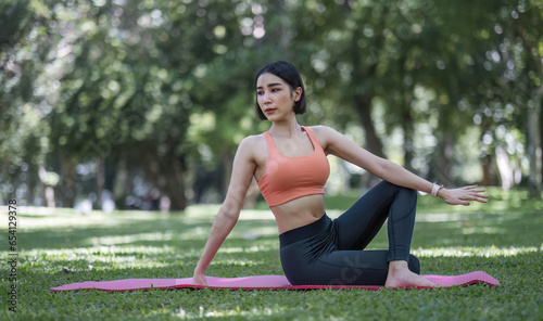 Attractive and charming Asian woman in her 30s in sportswear doing yoga poses, relaxing muscles. Asian woman practicing yoga in a beautiful green park