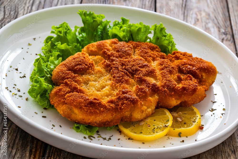 Crispy breaded seared chicken cutlet with lemon slices and fresh vegetables on wooden table
Crispy breaded seared chicken cutlet with lemon slices and fresh vegetables on wooden table