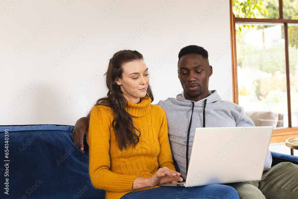 Diverse couple sitting on sofa using laptop at home Diverse couple sitting on sofa using laptop at home