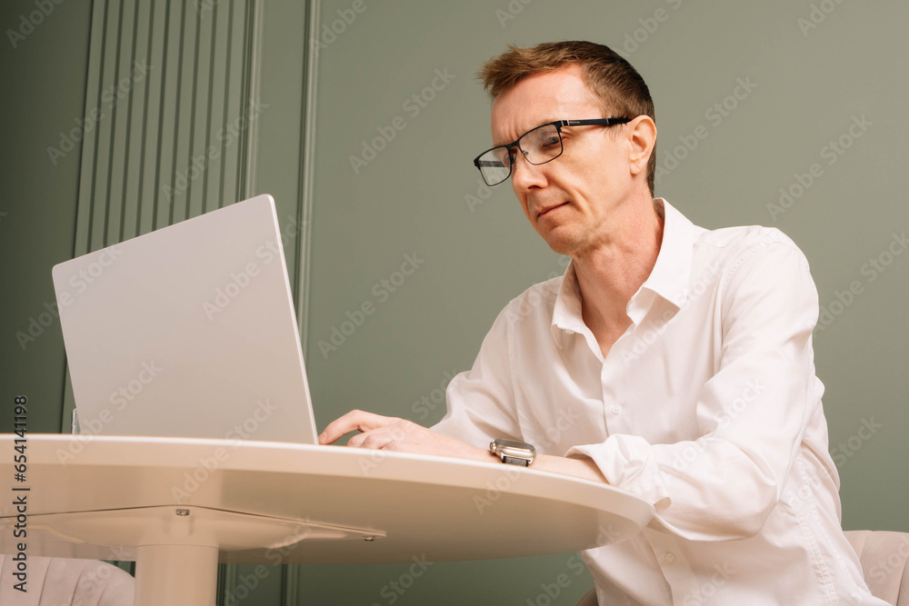 Hard-working business man in glasses, white shirt sitting at table and carefully examining case on screen of computer. Hard-working business man in glasses, white shirt sitting at table and carefully examining case on screen of computer.