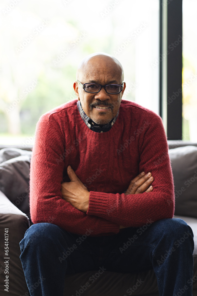 Portrait of happy senior biracial man wearing glasses sitting on sofa at home