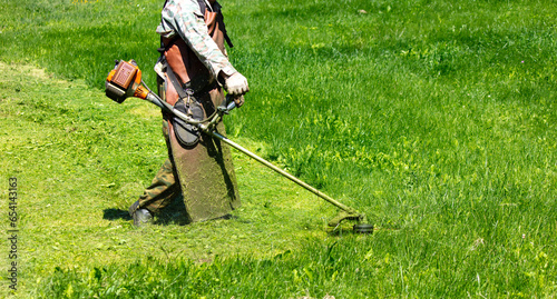 A man mows green grass with a petrol trimmer