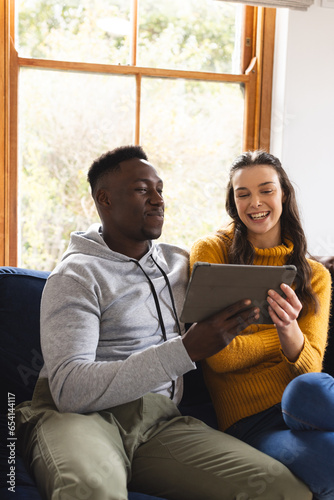 Happy diverse couple sitting on sofa using tablet at home