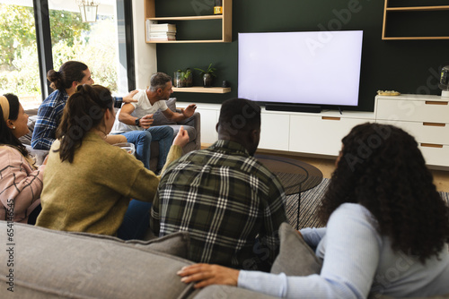 Fototapeta Naklejka Na Ścianę i Meble -  Excited diverse male and female friends watching sport on tv at home, copy space on screen