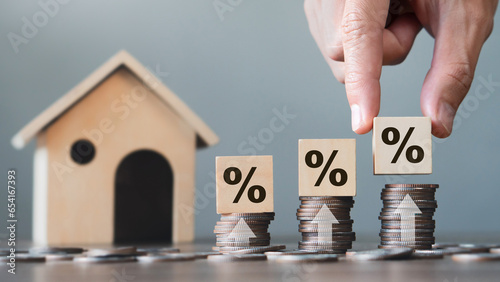 Hand holding wooden block with percentage symbol on stack coins and house model.Interest rates increase, home loan, mortgage, house tax. investment and asset management concept