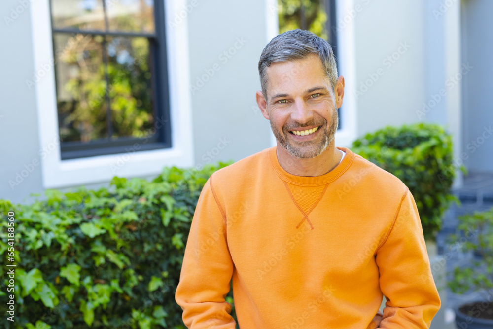 Happy caucasian man standing and smiling in front of house in sunny garden Happy caucasian man standing and smiling in front of house in sunny garden