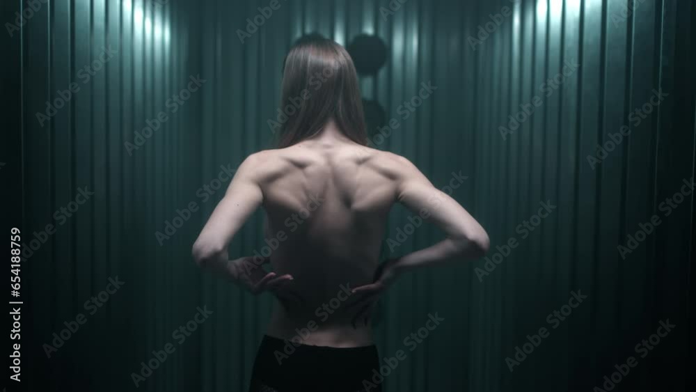 A beautiful slender brunette girl touches her bare back with her hands. Lean skinny female young body in the studio. Muscles, joints and tendons. Fashion video.