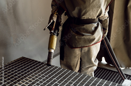 sandblasting a metal surface in a workshop close-up. a master in special clothing holds a sandblasting hose in his hands. working with sandblasting photo