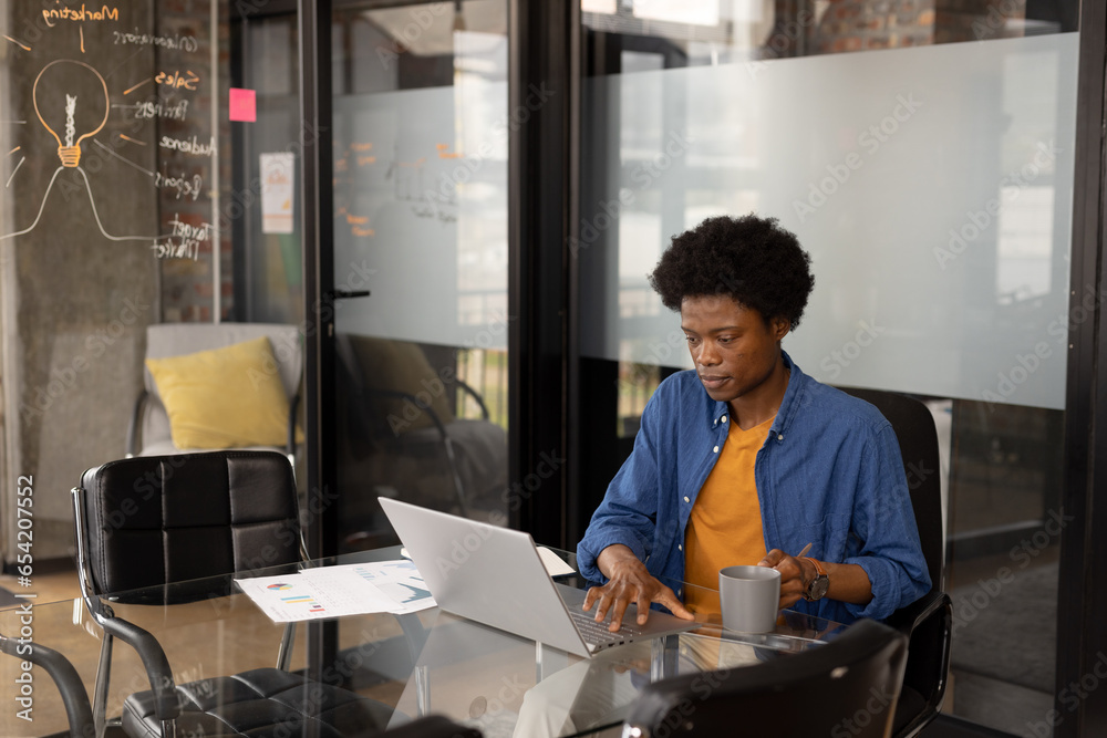 African american casual businessman using laptop and having coffee at home office, copy space African american casual businessman using laptop and having coffee at home office, copy space