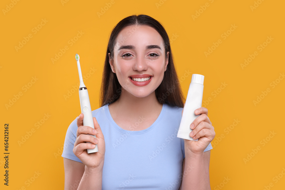 Φωτογραφία Happy young woman holding electric toothbrush and tube of toothpaste on yellow b