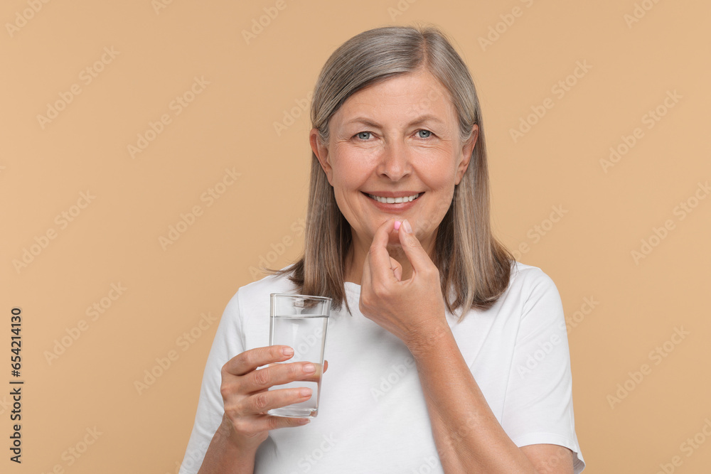 Senior woman with glass of water taking pill on beige background Senior woman with glass of water taking pill on beige background