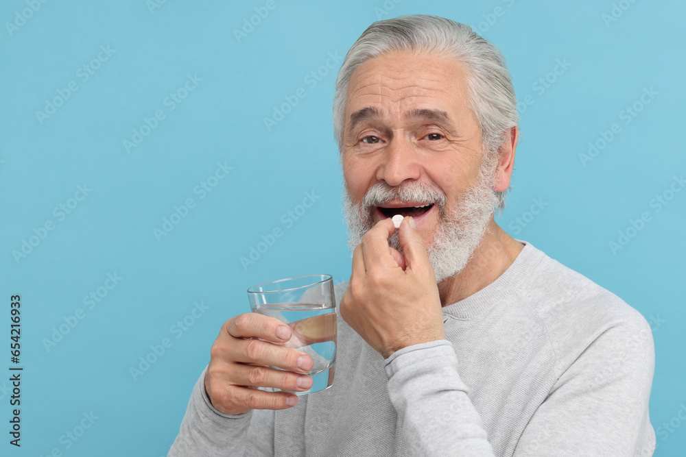 Senior man with glass of water taking pill on light blue background Senior man with glass of water taking pill on light blue background