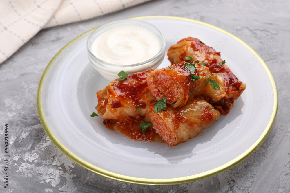 Delicious stuffed cabbage rolls served with sour cream on grey textured table, closeup Delicious stuffed cabbage rolls served with sour cream on grey textured table, closeup