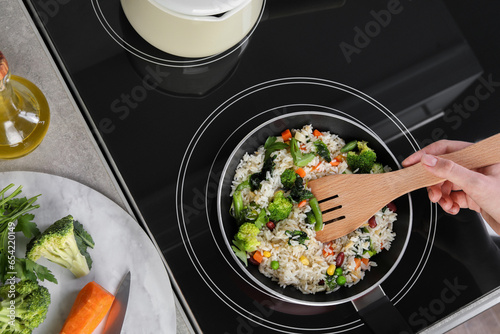 Woman frying rice with vegetables on induction stove, top view photo