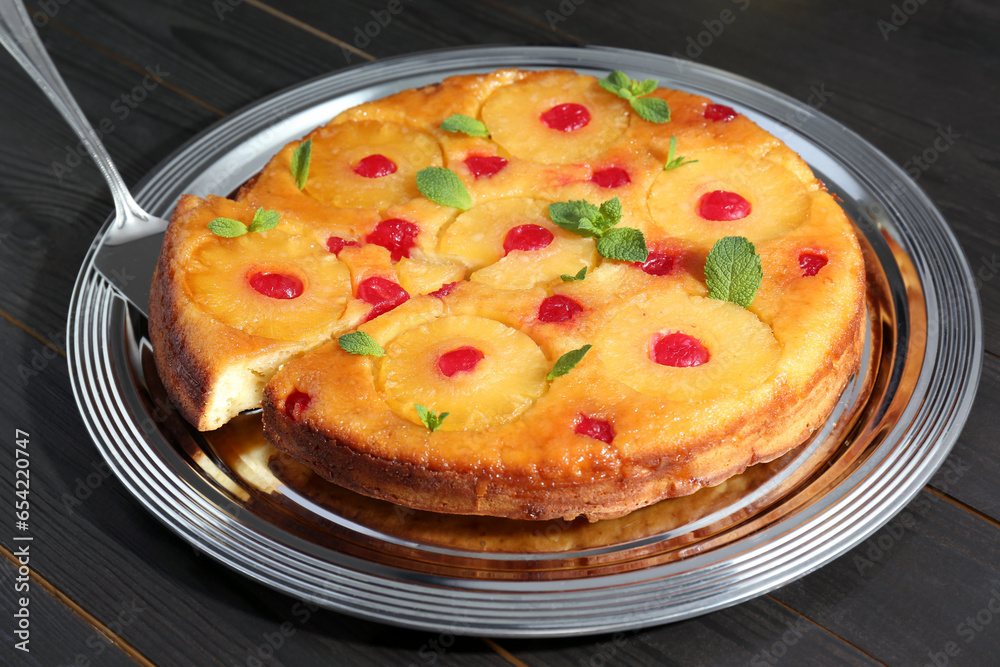 Taking piece of delicious cut pineapple pie with cherry and mint on dark wooden table Taking piece of delicious cut pineapple pie with cherry and mint on dark wooden table
