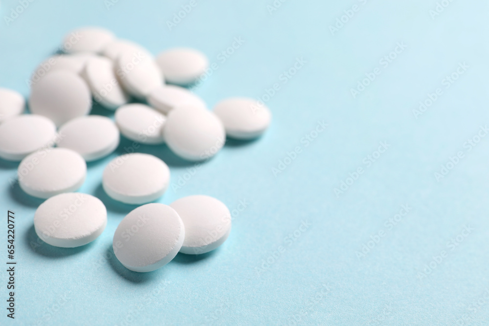 Many white pills on light blue background, closeup. Space for text
