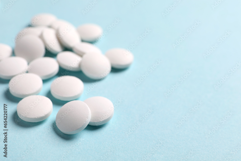 Many white pills on light blue background, closeup. Space for text Many white pills on light blue background, closeup. Space for text