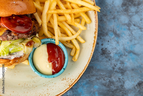 Beef burger with lettuce and pickles with fries and sauce on a gray-blue background