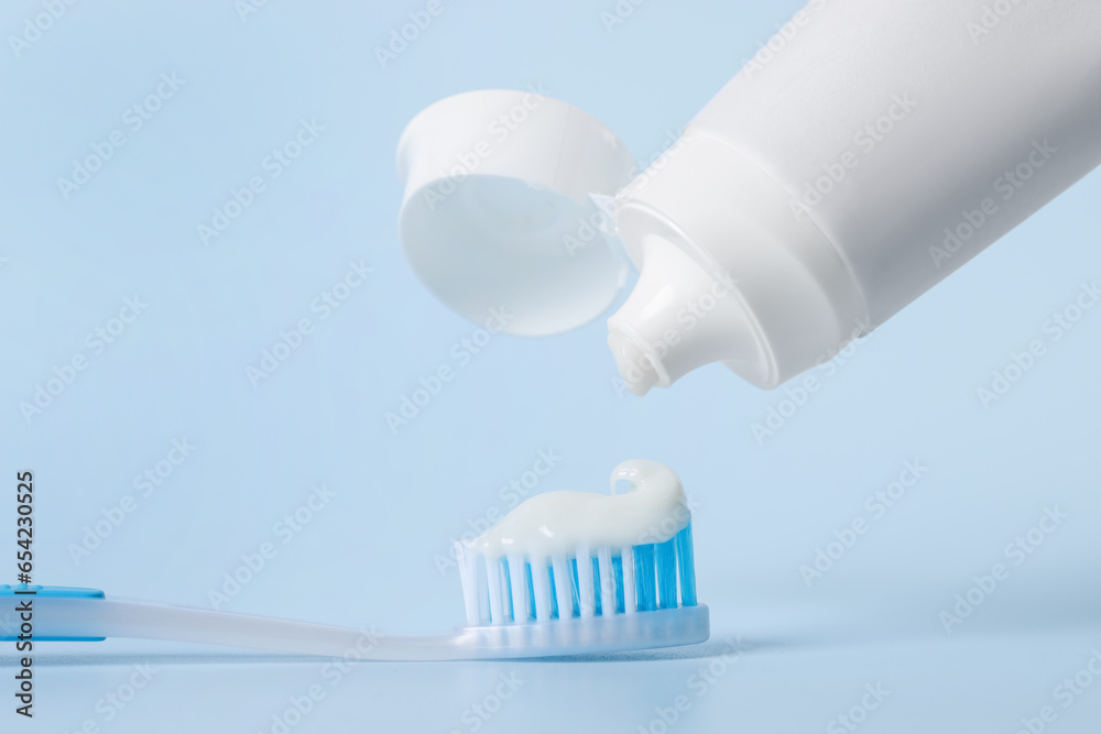 Applying paste on toothbrush against light blue background, closeup Applying paste on toothbrush against light blue background, closeup