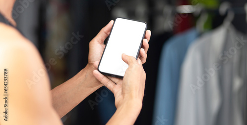 lifestyle man holding  smartphone with white screen in clothing room and shirts  background, Smartphone design application online shopping clothes concept