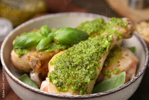 Delicious fried chicken drumsticks with pesto sauce and basil in bowl, closeup