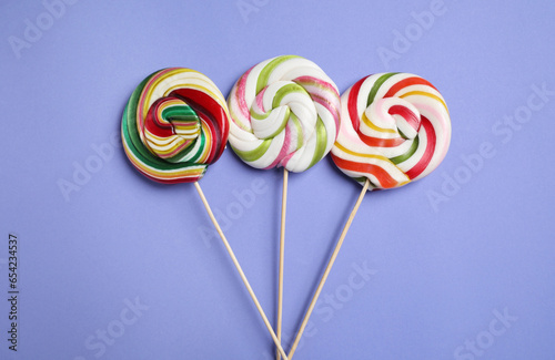 Sticks with different colorful lollipops on violet background, flat lay