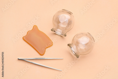 Glass cups, gua sha and tweezers on light coral background, flat lay. Cupping therapy