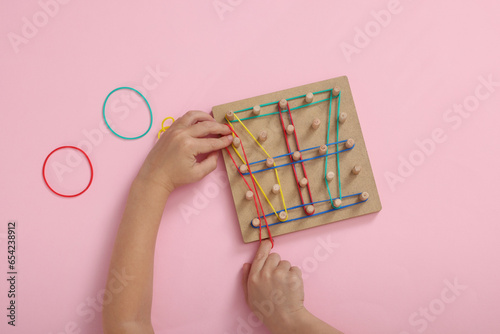 Motor skills development. Boy playing with geoboard and rubber bands at pink table, top view photo