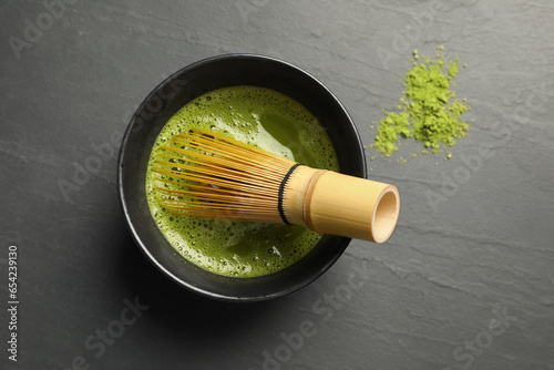 Cup of fresh matcha tea with bamboo whisk on black table, flat lay