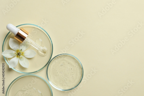 Petri dishes with samples of cosmetic oil, pipette and beautiful flower on beige background, flat lay. Space for text