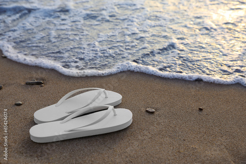 Stylish white flip flops on sand near sea. Space for text